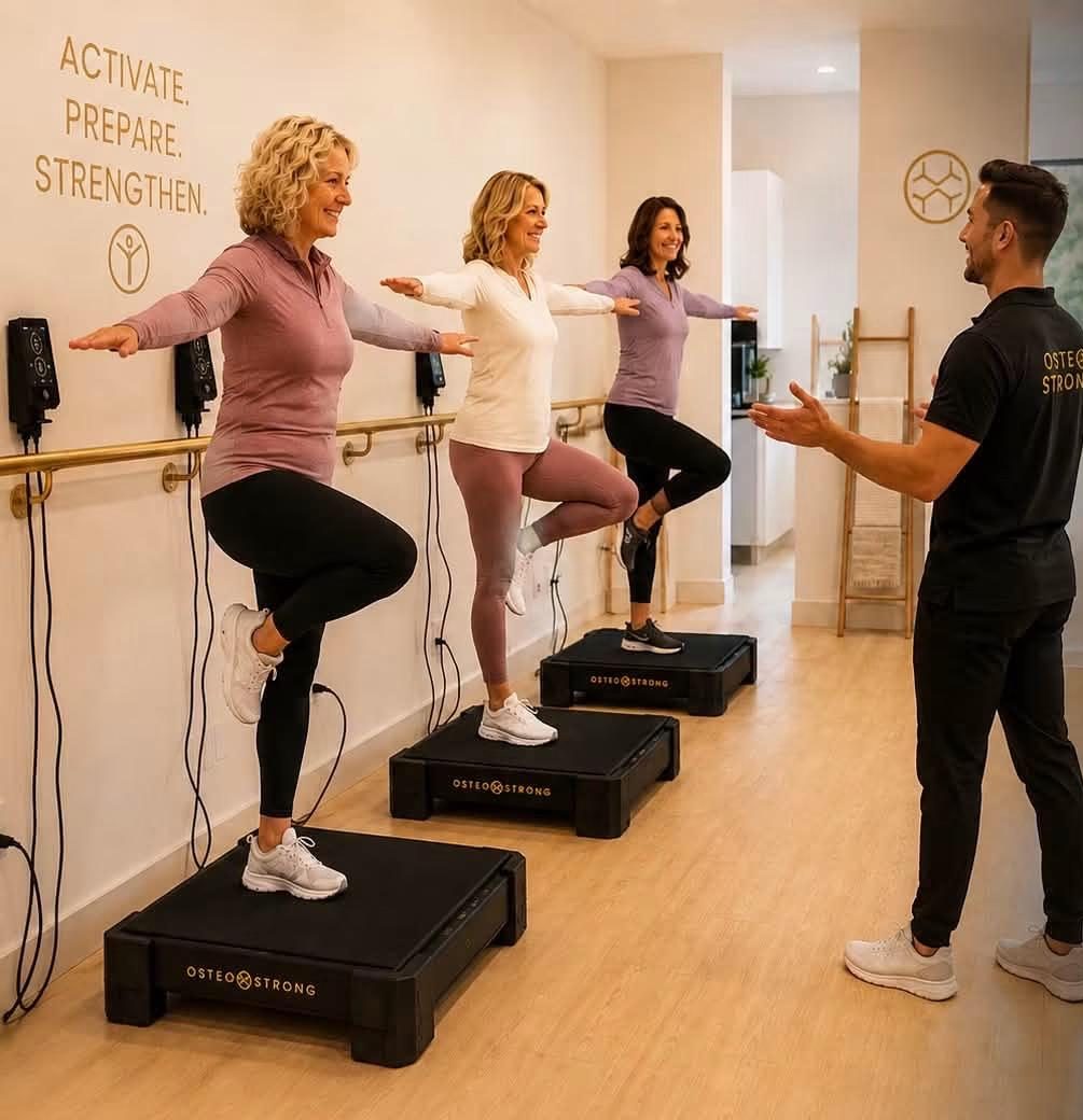 Three members balancing on one leg on OsteoStrong Vibration Plates while a coach guides them